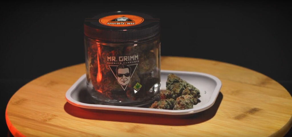 An ounce of Peanut Butter Breath by Mr. Grimm bathed in orange light on a product lazy susan, with a rolling tray and some loose nugs.